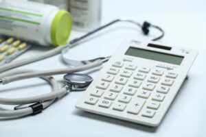 Calculadora, estetoscópio e medicamentos sobre superfície branca, representando a gestão de custos na saúde